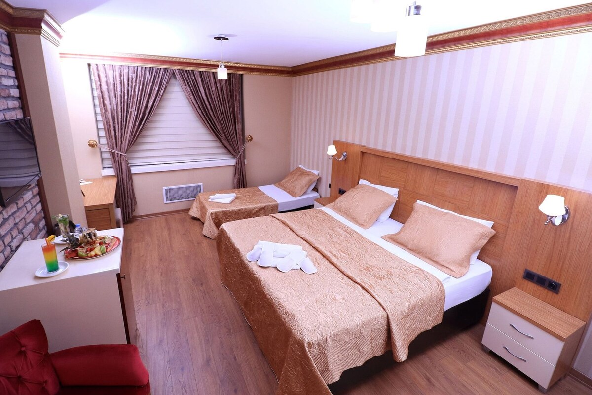 A hotel room with two beds, a small table with a drink and fruit, a red chair, and a brick wall.