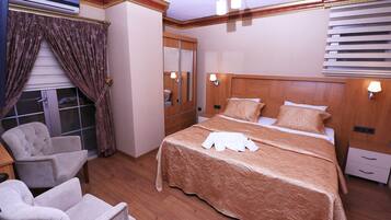 Quarto de hotel com uma cama grande, duas poltronas, cabeceira de madeira, um espelho e uma janela com cortinas.