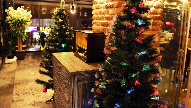 A lobby with a brick pillar, a wooden reception desk, and two Christmas trees with lights.