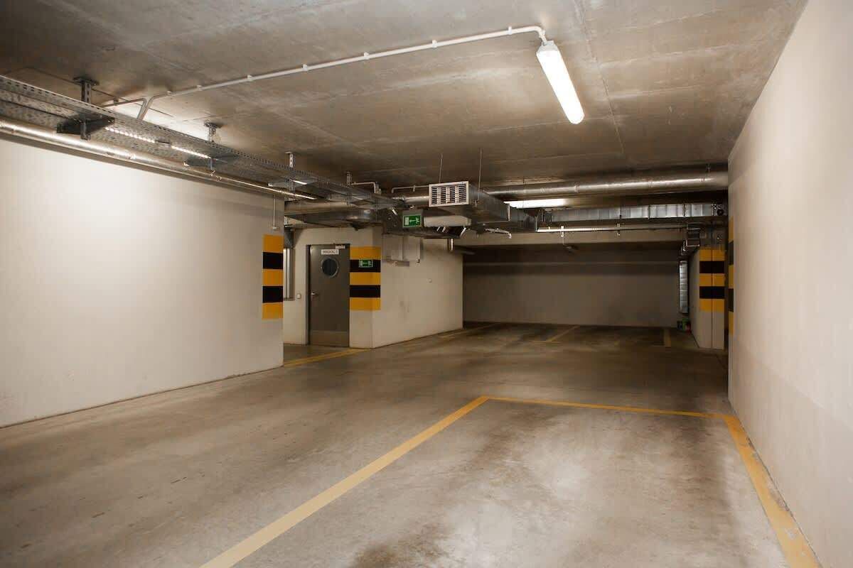 Un estacionamiento vacío con pisos de concreto, líneas amarillas y letreros de salida de emergencia.