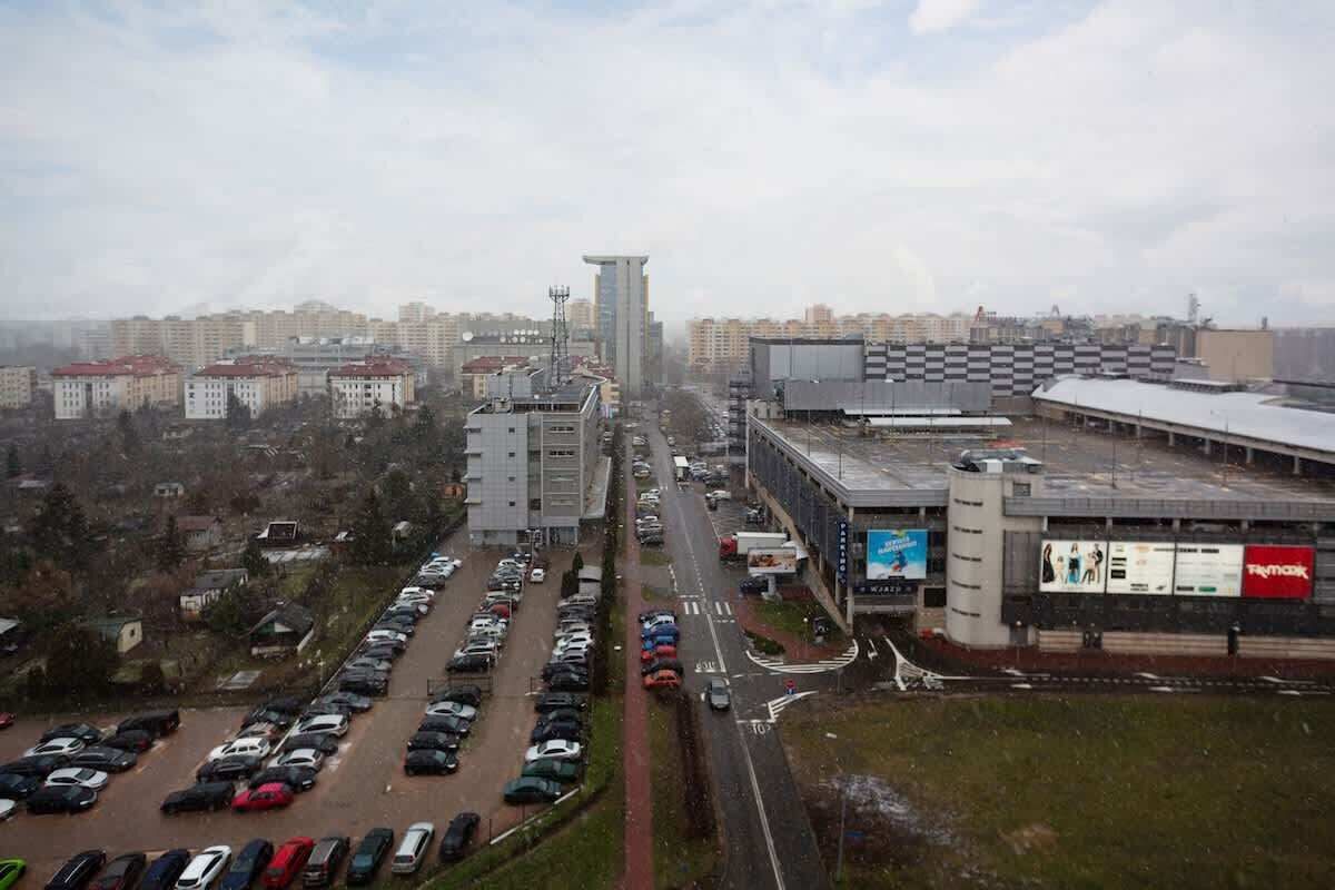 A parking lot with multiple cars, a large building with a flat roof, and a smaller structure with a red roof.