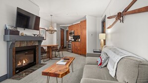 A modern living room with a fireplace, a dining area, a kitchen, and a large TV.