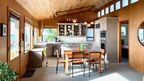 Une cuisine moderne avec des meubles en bois, un coin repas comprenant une table et des chaises en bois, et une vue sur l’extérieur grâce à de grandes fenêtres.