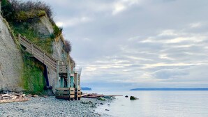 Un bâtiment situé sur la côte, doté d’un escalier menant à une terrasse en bois, d’où l’on peut admirer une mer calme.