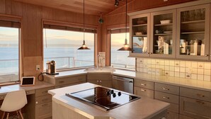 Une cuisine moderne avec des meubles en bois, un grand îlot central doté d’une plaque de cuisson et une vue sur la mer.