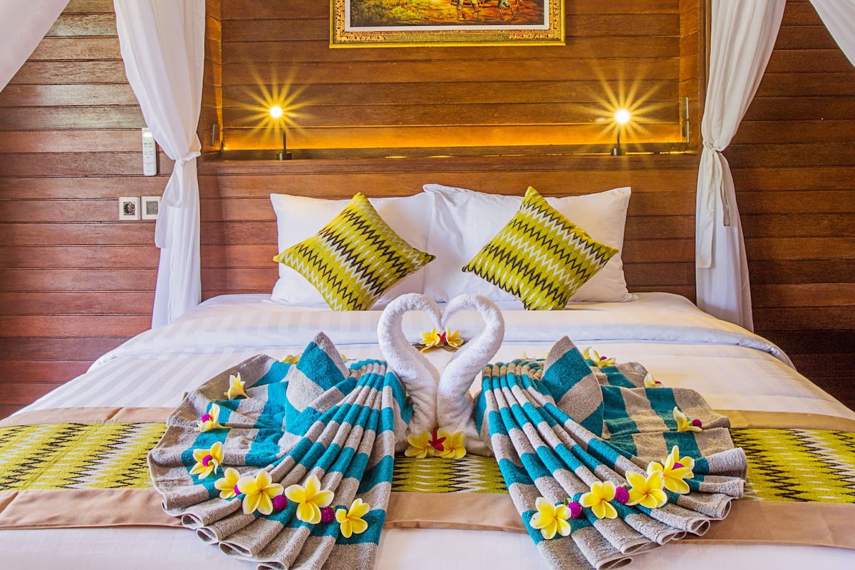 A bed with a canopy, pillows, and a towel arrangement.