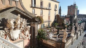 A courtyard with ornate stone balustrades, a fountain, and classical statues.