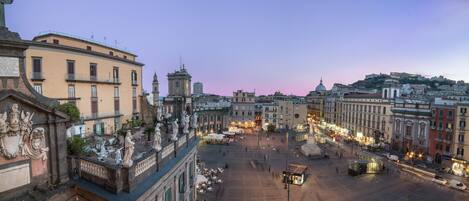 Una plaza histórica con arquitectura clásica, que incluye estatuas y fachadas decoradas, rodeada de edificios con balcones y farolas.