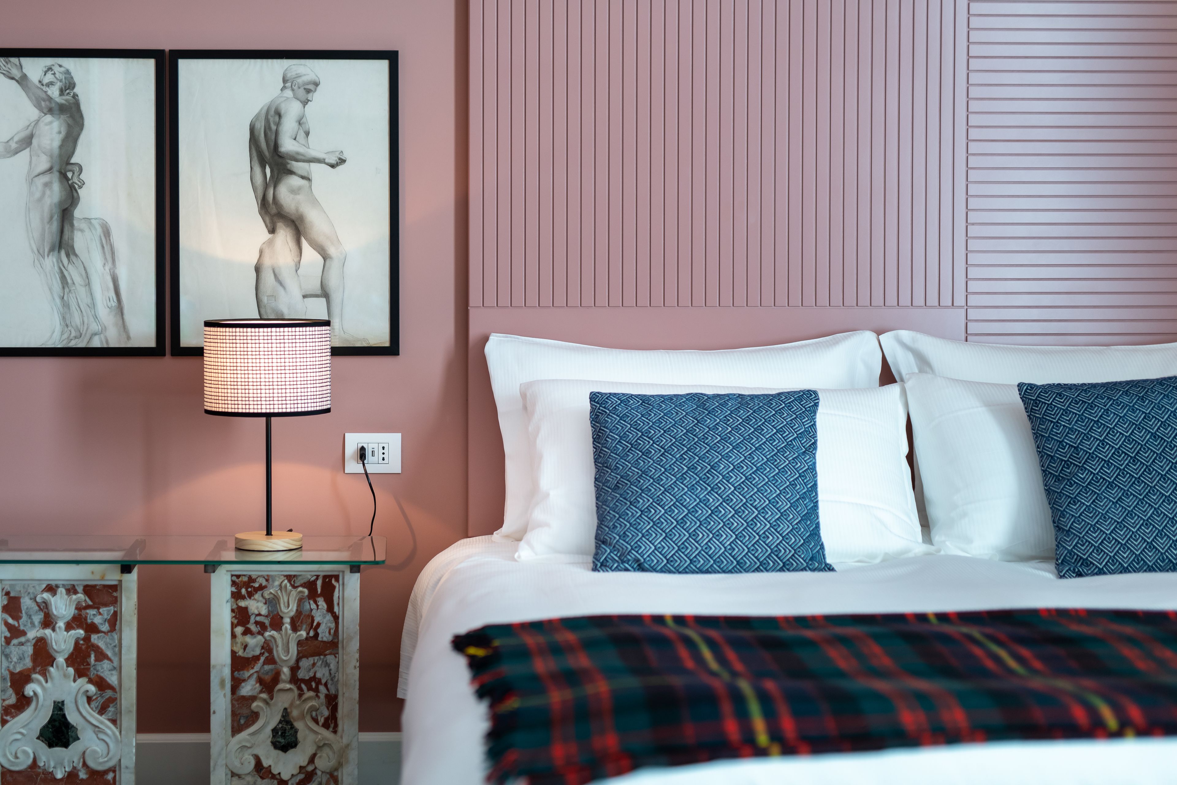 Ein ordentlich bezogenes Bett mit weißen und blauen Kissen, einer Karo-Decke und zwei gerahmten Kunstwerken an der Wand.