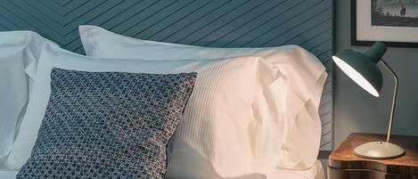A neatly made bed with patterned pillows, a bedside table with a lamp, and a wall with a geometric pattern.