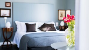 A bedroom with a bed, pillows, a nightstand, a vase with flowers, and framed pictures on the wall.