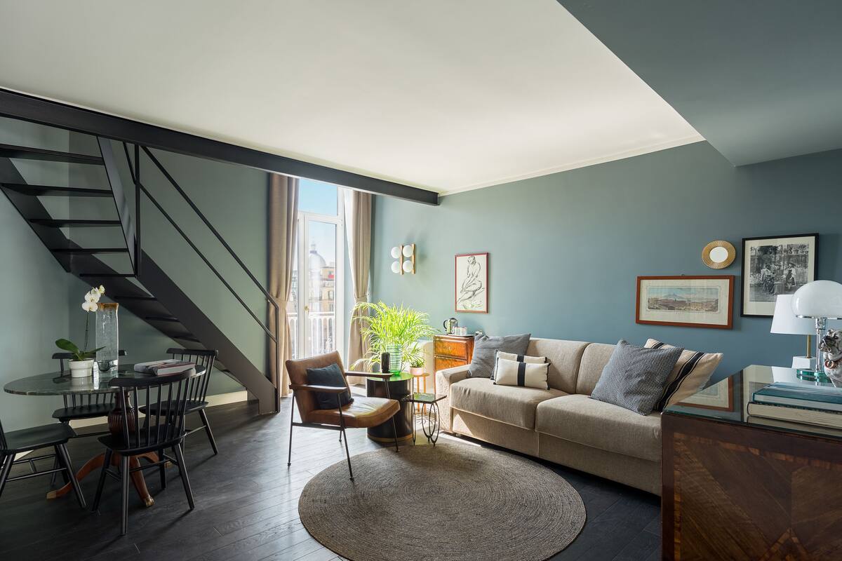 A modern living room with a staircase, a round dining table, a sofa, and a coffee table.