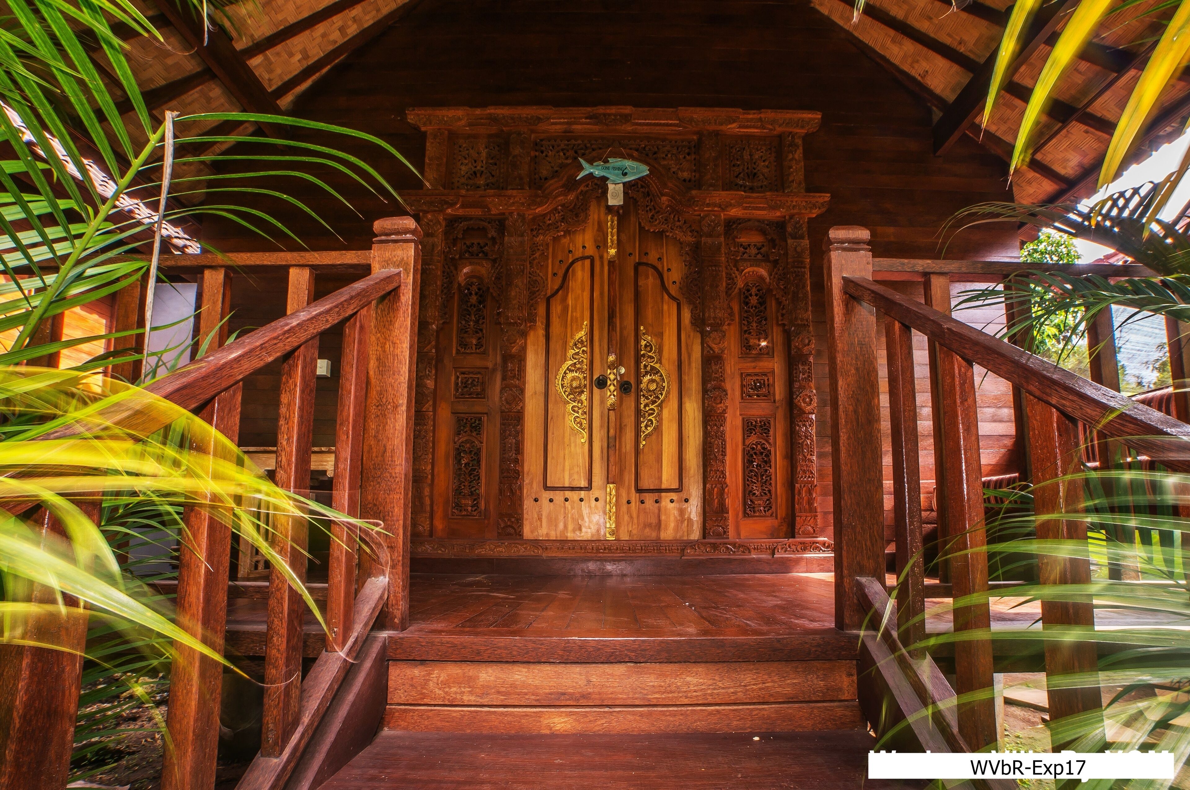 A wooden staircase leading to a door with intricate carvings and a fish hanging above it.