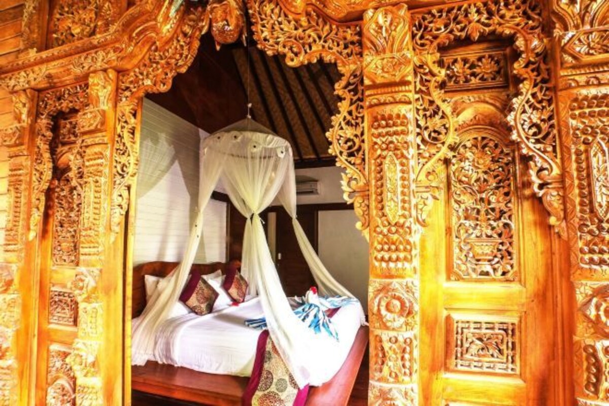 A room with a bed under a canopy, ornate wooden carvings, and a traditional design.