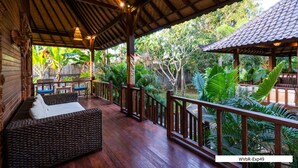Een overdekt terras met houten meubilair en uitzicht op weelderige begroeiing.