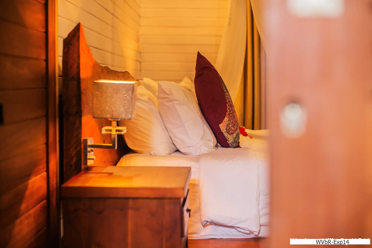 Una habitación acogedora con cabecera de madera, lámpara de noche y cama bien hecha con almohadas blancas y burdeos.