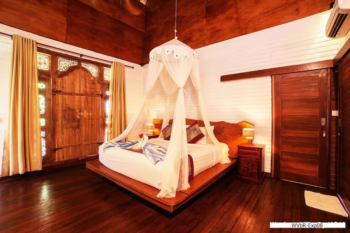 Un espacioso dormitorio con cama con dosel, suelo de madera y un gran ventanal con cortinas.