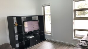 A living room with a black entertainment unit, a flat-screen TV, and a window with a view of trees.
