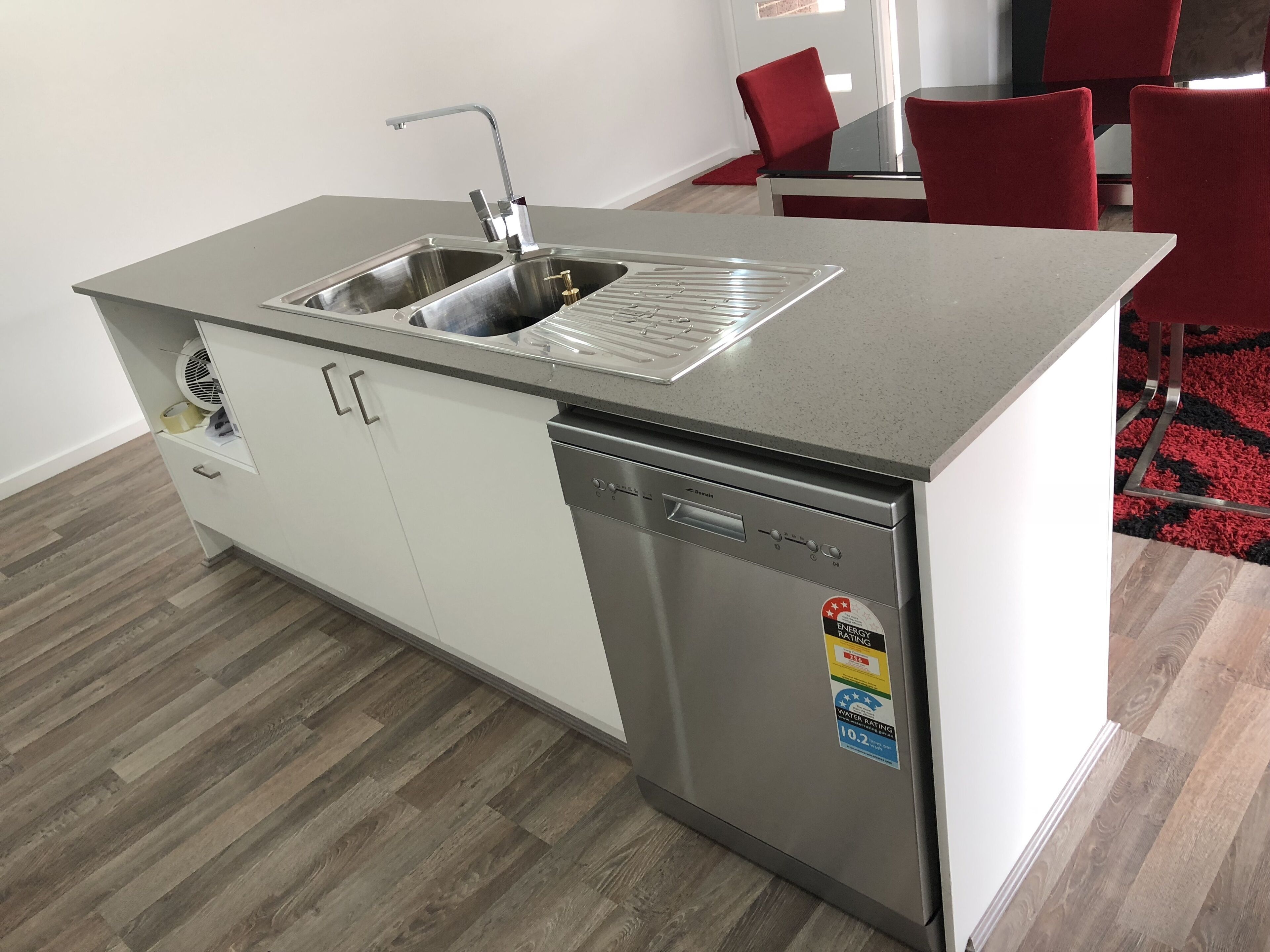 Een kleine keuken met een roestvrijstalen spoelbak, een vaatwasser en een klein kastje.