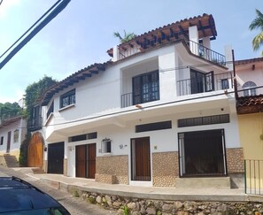 A two-story house with a balcony, stone facade, and a wooden door.
