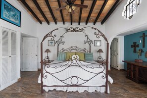 A four-poster bed with a decorative headboard, two bedside lamps, and a ceiling fan in a room with a tiled floor and a wooden ceiling.