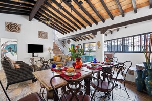 A spacious living area with a dining table set for four, surrounded by wicker furniture and metal chairs.
