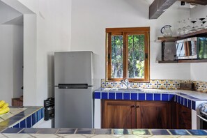 A kitchen with a refrigerator, a sink, wooden cabinets, and a window with a view of greenery.