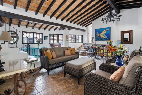 A spacious living area with a high ceiling, wicker furniture, and a large painting of a sea turtle.