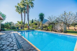 A swimming pool with stone tiles, surrounded by palm trees and a clear blue sky.