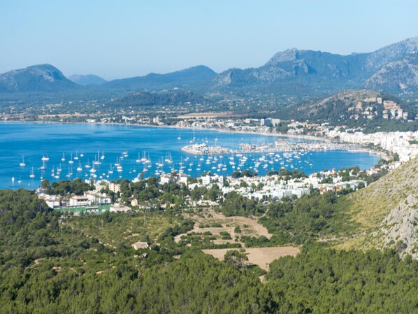 A coastal town with a marina filled with boats, surrounded by mountains and greenery.