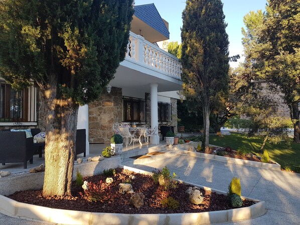Una casa moderna con fachada de piedra, mobiliario exterior y un jardín cuidado.