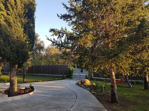 Un sendero pavimentado que lleva a un parque infantil con valla y árboles.