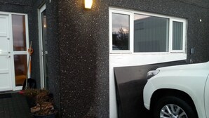 Et hus med en garageport, en hvid bil parkeret udenfor, og en potteplante ved indgangen.