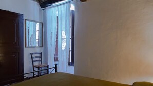 A room with a bed, a chair, a window with curtains, and a door. - Historic house in the center of Cortona (Cortona)