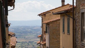 A narrow street with stone buildings, a visible archway, and a distant view of the countryside. - Historic house in the center of Cortona (Cortona)