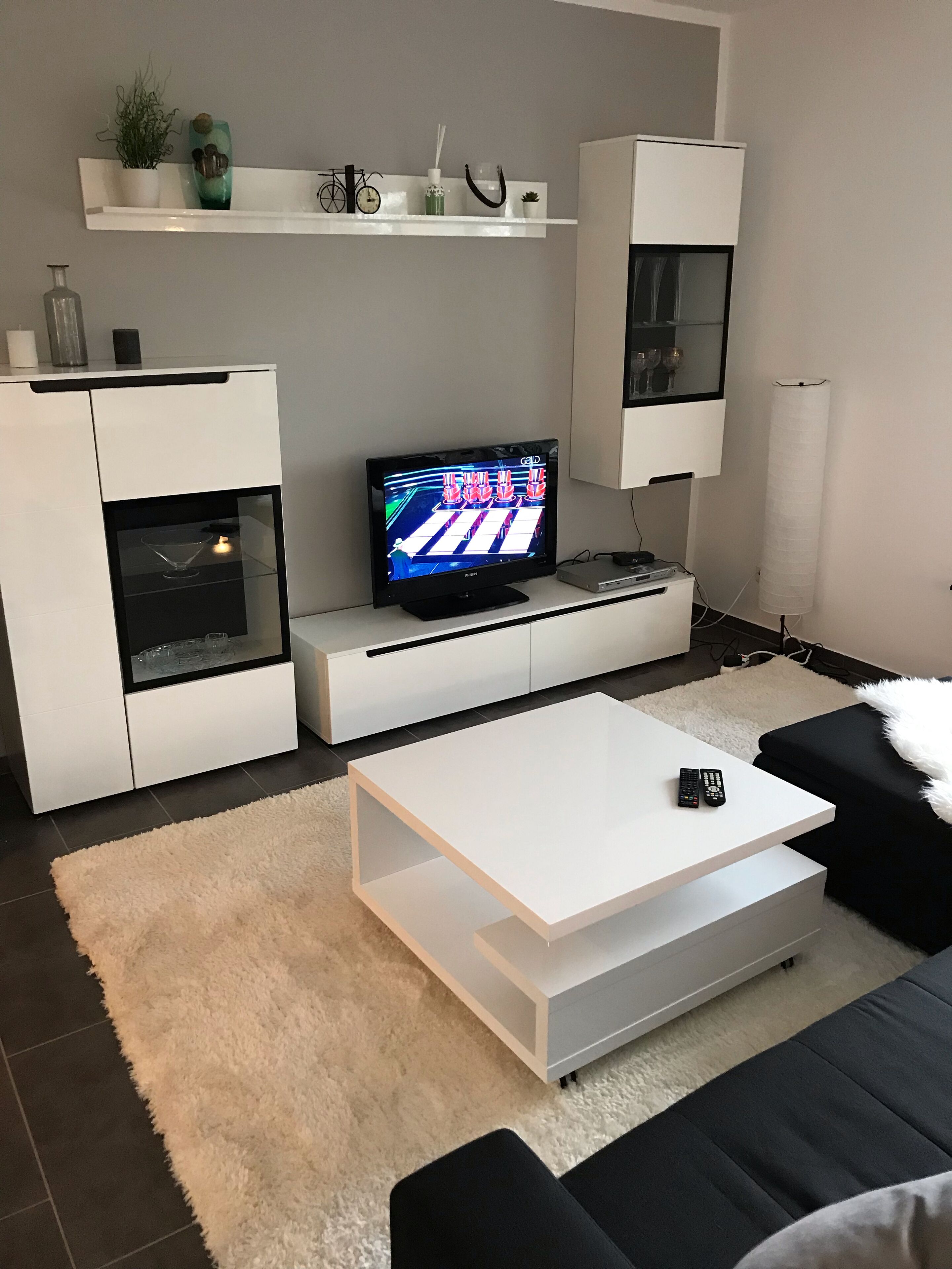 Een moderne woonkamer met een flatscreen televisie, witte kasten, een witte salontafel en een zwarte bank.