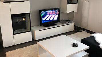 Een moderne woonkamer met een flatscreen televisie, witte kasten, een witte salontafel en een zwarte bank.