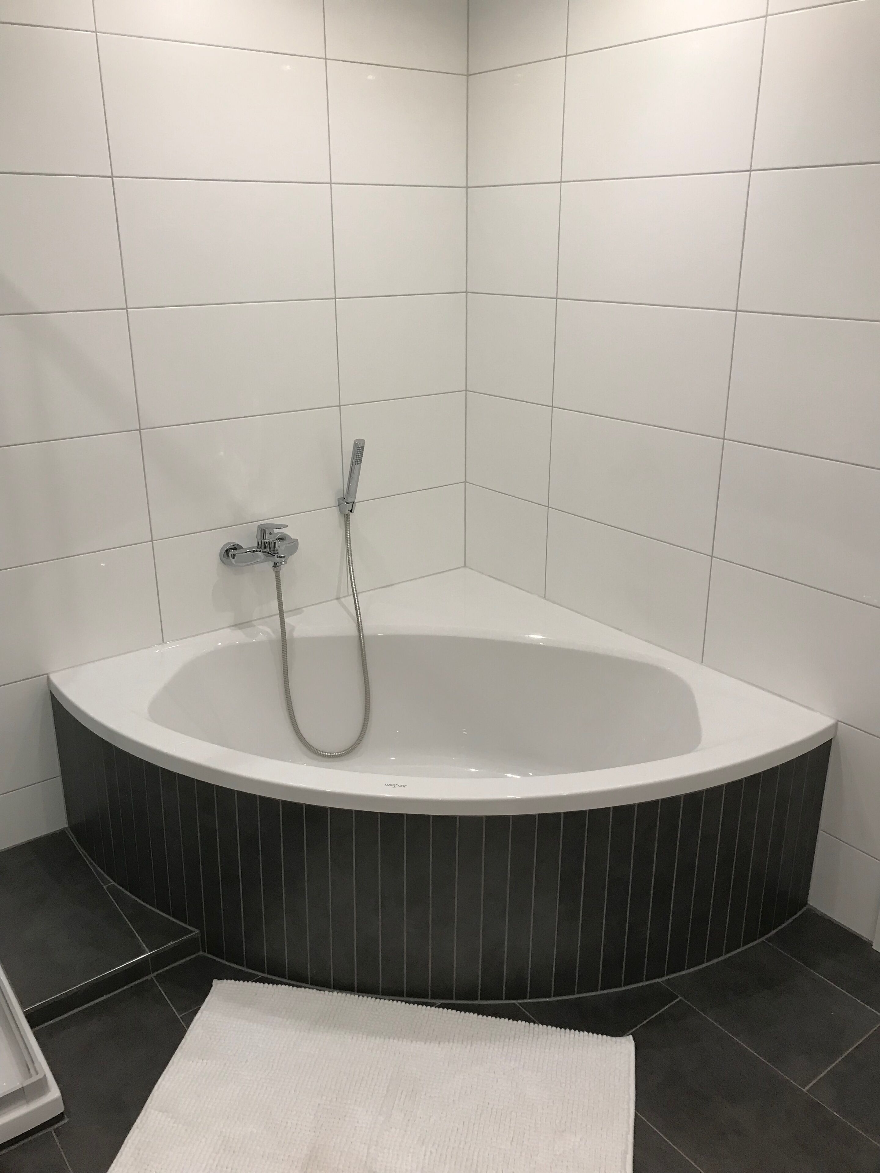 A modern bathroom with a freestanding bathtub, a handheld showerhead, and dark striped tiles.