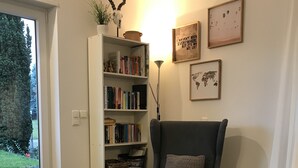 Ett mysigt vardagsrum med en grå fåtölj, en bokhylla full av böcker, ett litet runt bord med en växt och en världskarta på väggen.