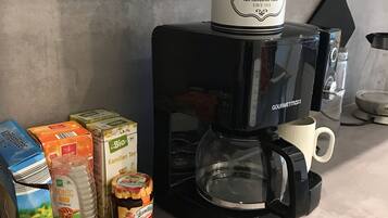 Une machine à café avec une verseuse sur le dessus, un mousseur à lait et divers produits à base de café et de thé disposés sur un plan de travail de cuisine.