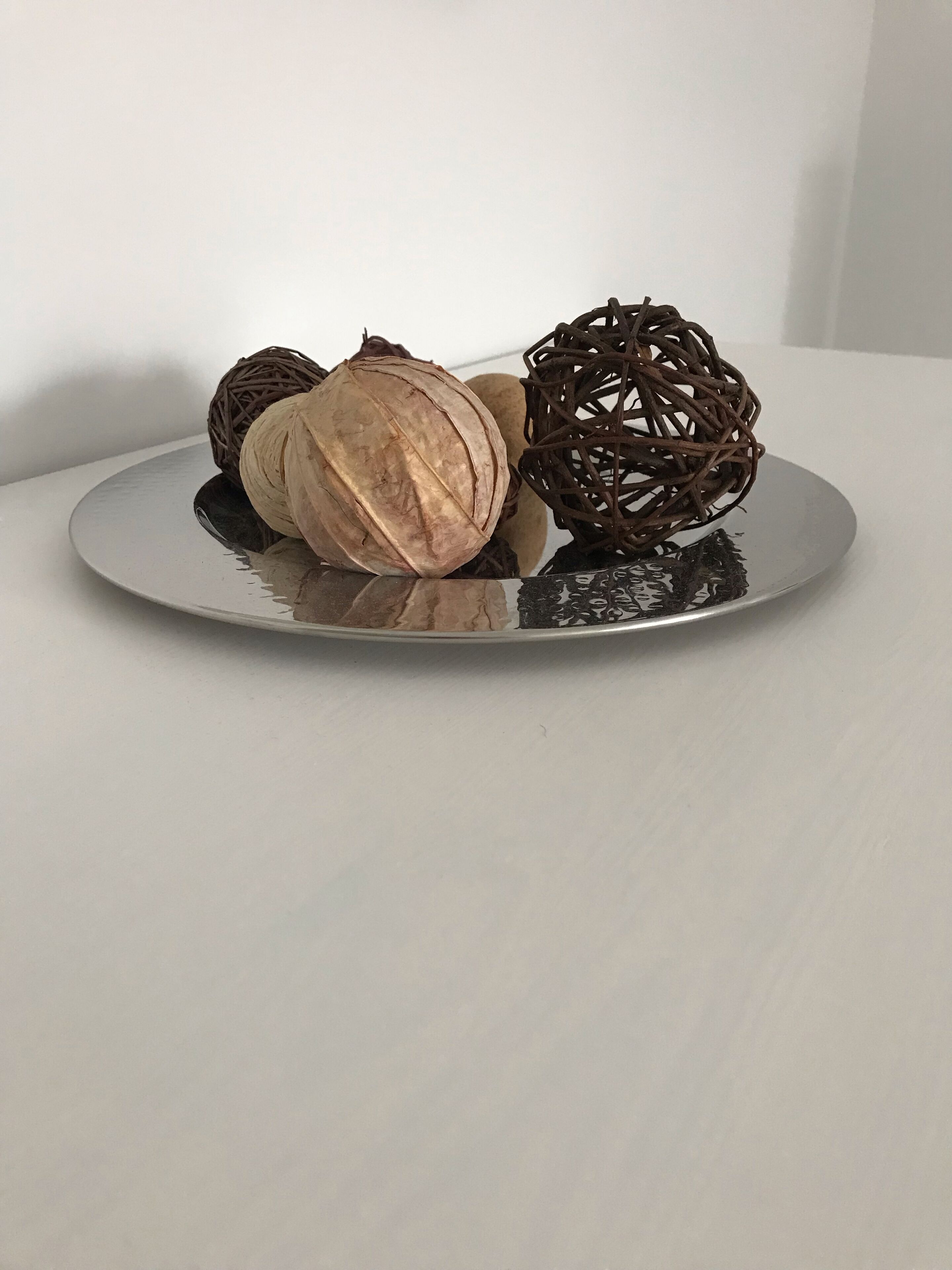 Ein Teller mit einer gewebten Kugel und einer Walnuss auf einer spiegelnden Oberfläche.
