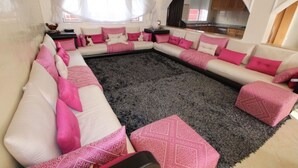 Un salon doté d’un grand canapé d’angle, d’un tapis à poils longs de couleur grise et de coussins roses et blancs.