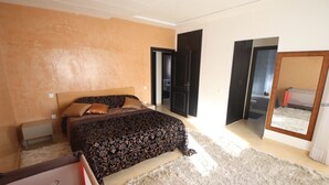 Une chambre à coucher comprenant un lit, une table de chevet, un miroir et une porte donnant sur une autre pièce.