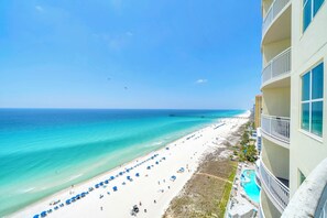 A beach view with a pier, a pool, and a building with balconies.