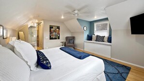 Un dormitorio con cama, una silla, ventana con persianas, ventilador de techo y televisión montada en la pared.