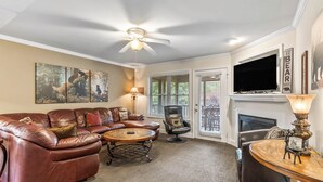 A living room with a leather sofa, a coffee table, a fireplace, and a television. - Sleeping Bear Condo - Downtown Helen, GA (Helen)