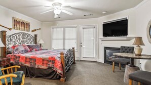 A hotel room with a bed, a television, a fireplace, a dining table, and a ceiling fan. - Sleeping Bear Condo - Downtown Helen, GA (Helen)