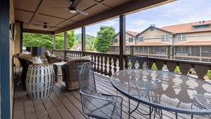 A covered outdoor area with a table and chairs, a ceiling fan, and a view of residential buildings in the background. - Sleeping Bear Condo - Downtown Helen, GA (Helen)