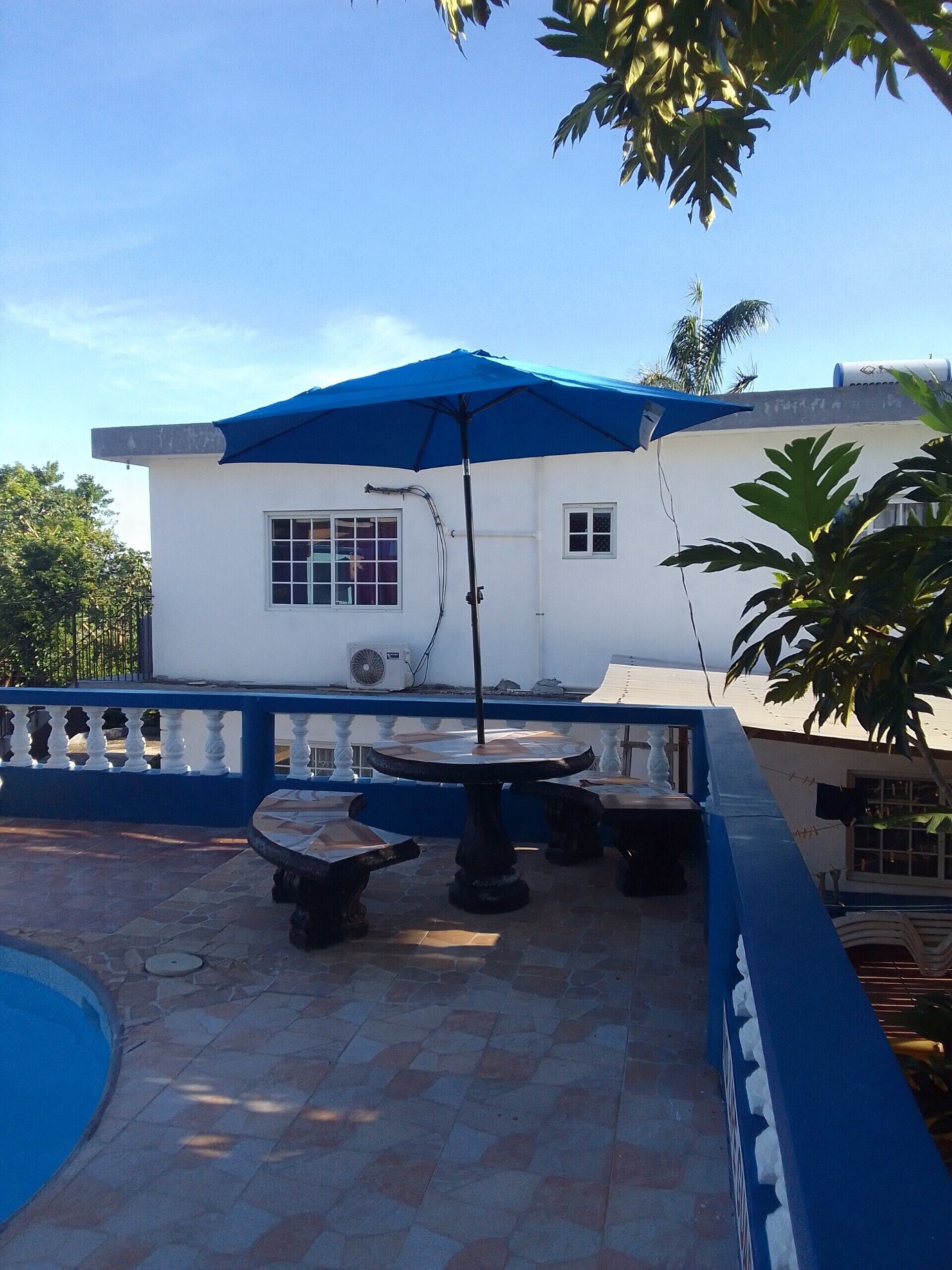 Un espace patio avec un parasol bleu, une table ronde et un bâtiment blanc en arrière-plan.