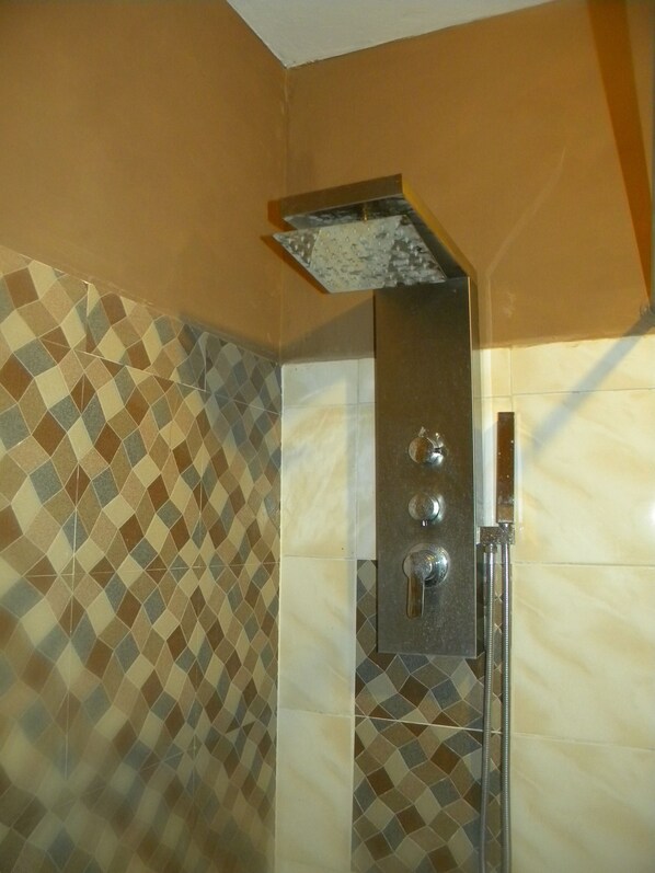 A bathroom with a patterned tile wall, a shower enclosure, and a wall-mounted faucet.